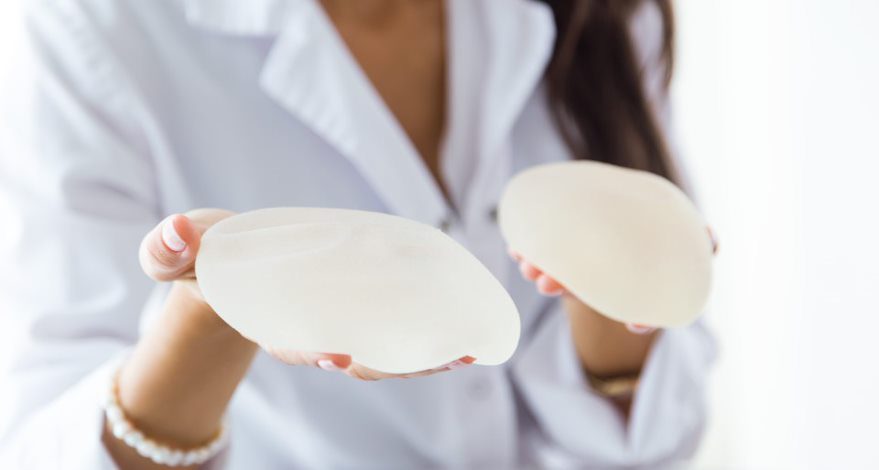 Woman holds a breast implant in each hand.