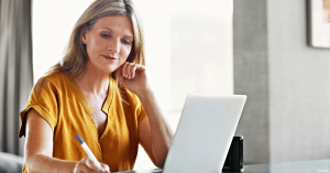 Woman on laptop jotting down notes