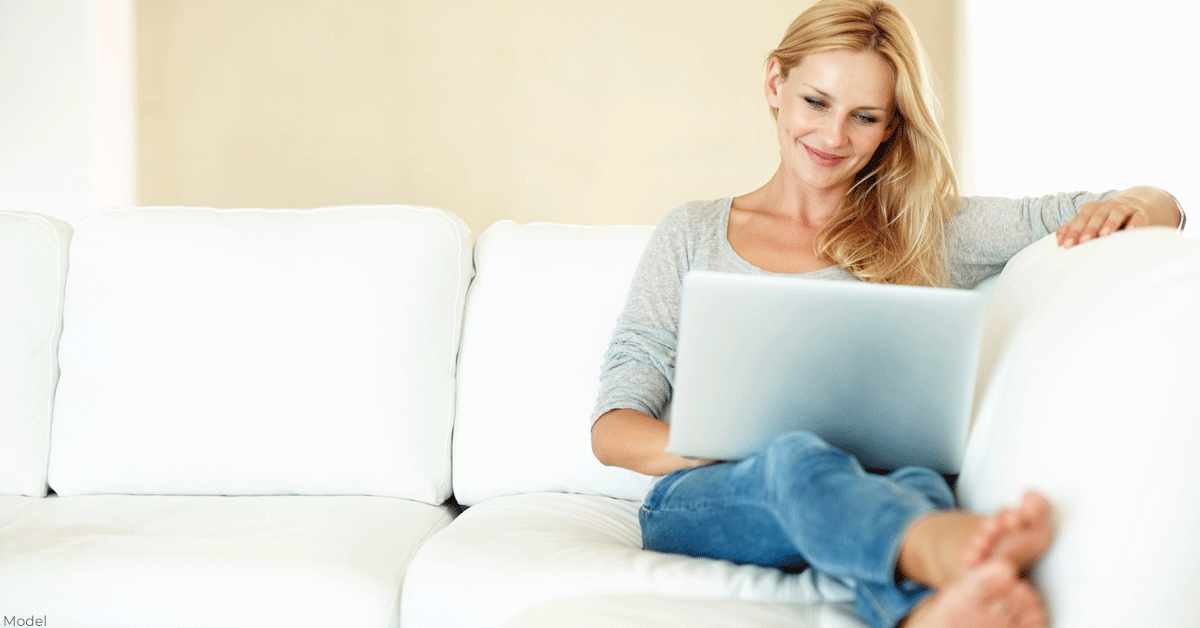 Woman on couch researching which plastic surgeon to choose for her breast augmentation.