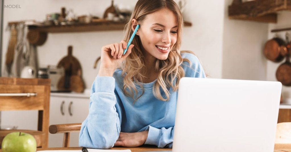 Woman (model) looking at her laptop and smiling.