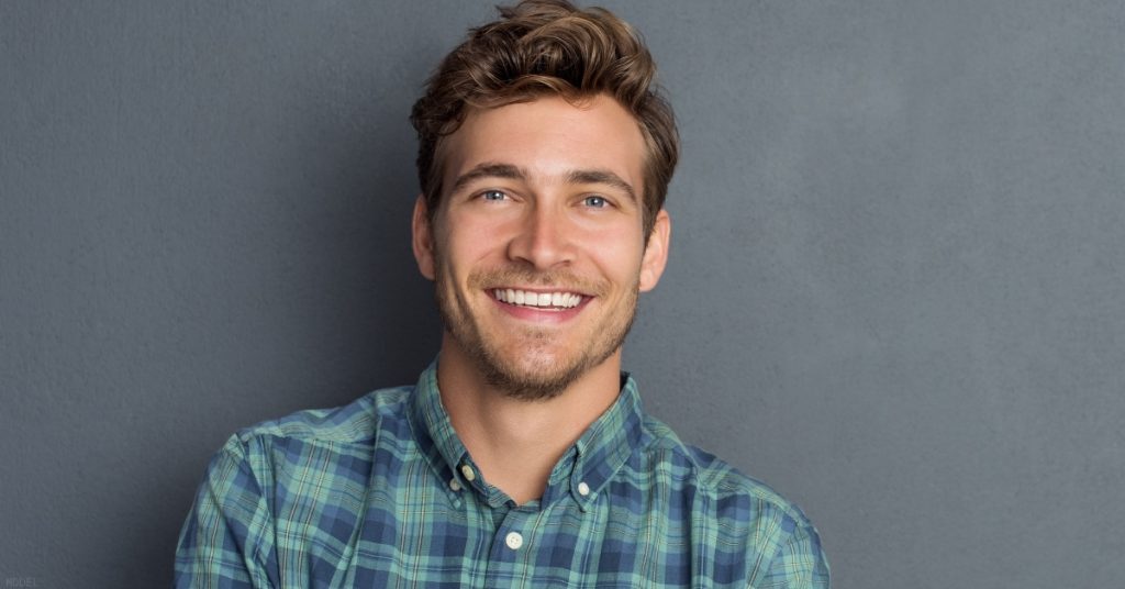 Man in plaid shirt standing against gray wall (model)